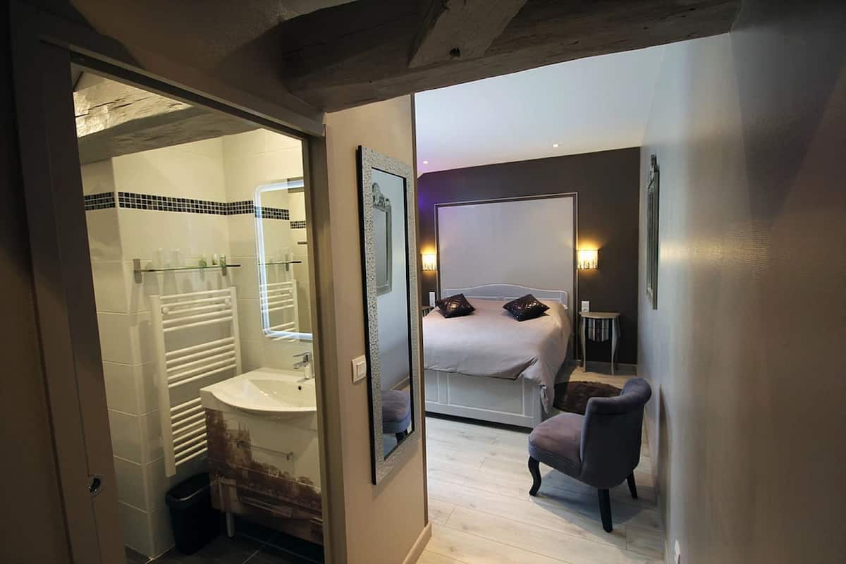 Una habitación de hotel con baño, una cama, una silla y una pequeña mesa.