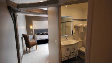 Un dormitorio con una cama, una silla y una mesita de noche. El piso es de madera y la pared es blanca.
