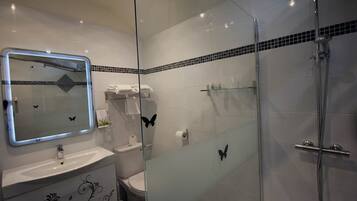 Un baño moderno con ducha envuelta en vidrio, un lavamanos blanco con diseños decorativos y un espejo con una calcomanía de mariposa.
