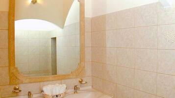 Un bagno con uno specchio grande, un lavandino con dettagli dorati e un portascopevoli.