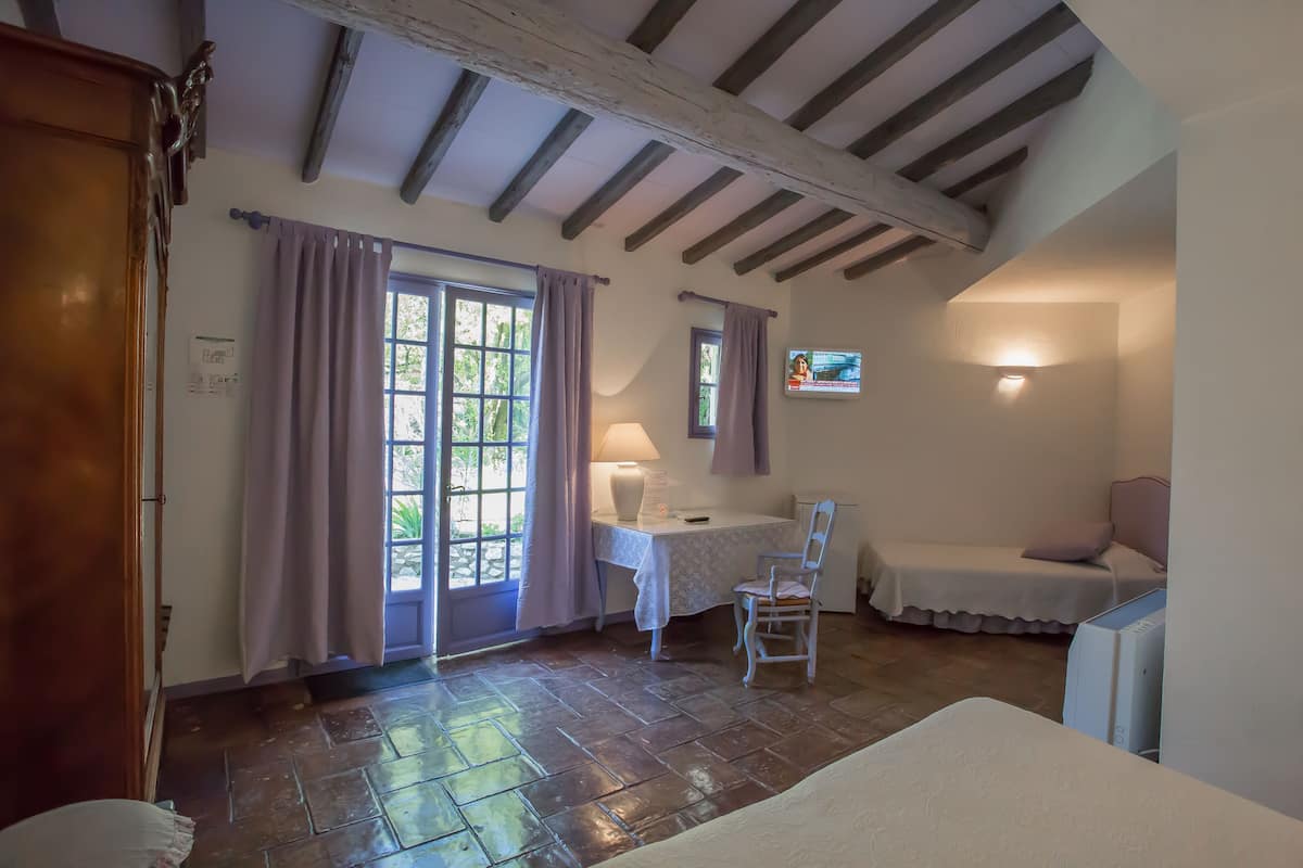 A bedroom with a bed, a desk, a chair, a TV, and a window with curtains.