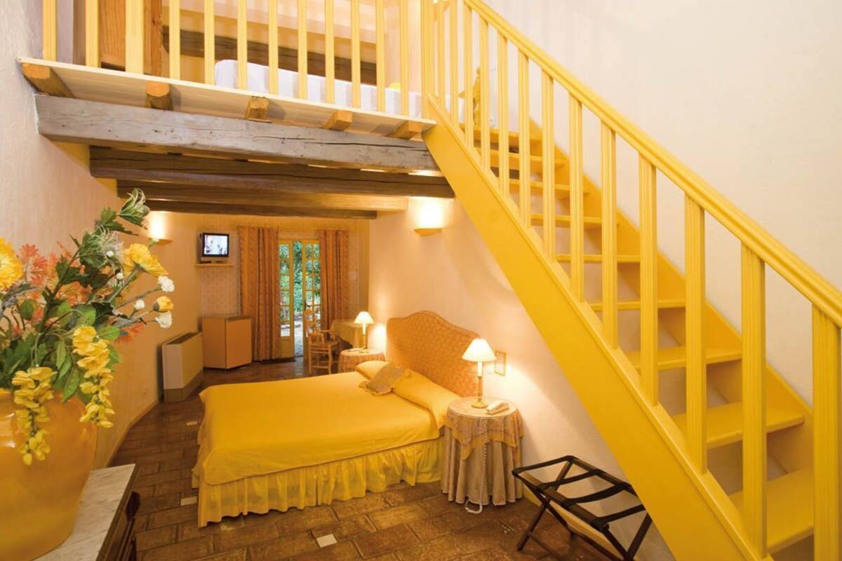 A hotel room with a bed, a small table, a chair, a TV, and a staircase.