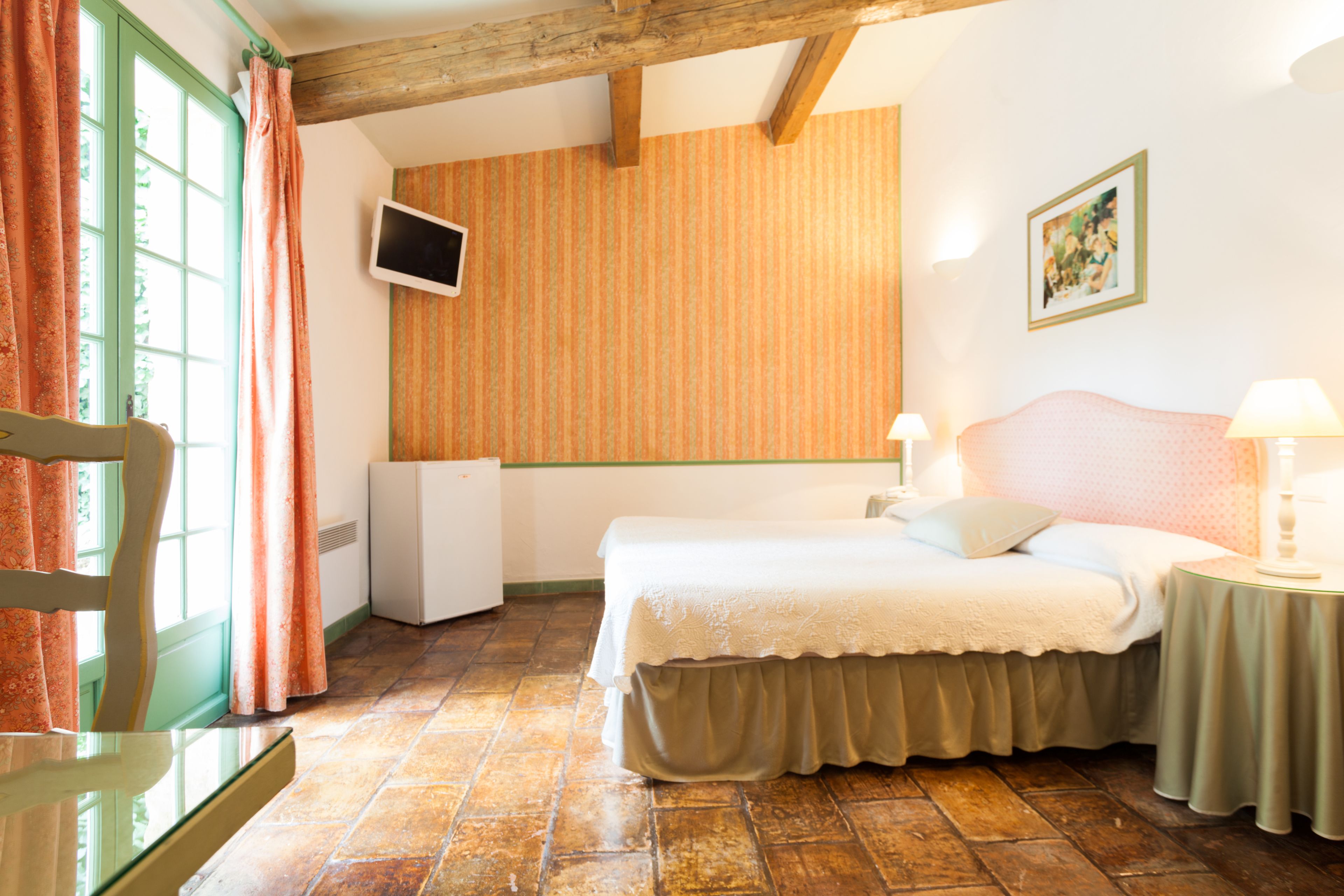A bedroom with a bed, bedside tables, a window with curtains, a wall-mounted TV, and a framed picture.