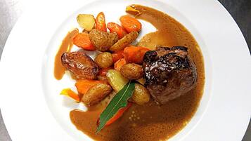 A plate of food with a steak, carrots, and potatoes in a brown sauce.