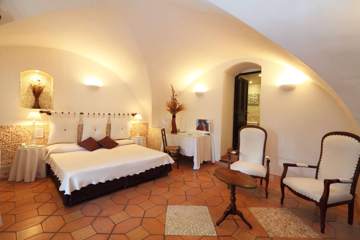 A bedroom with a large bed, a desk, two chairs, and a small table.