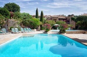 Une piscine avec des chaises longues et un bâtiment en pierre en arrière-plan.