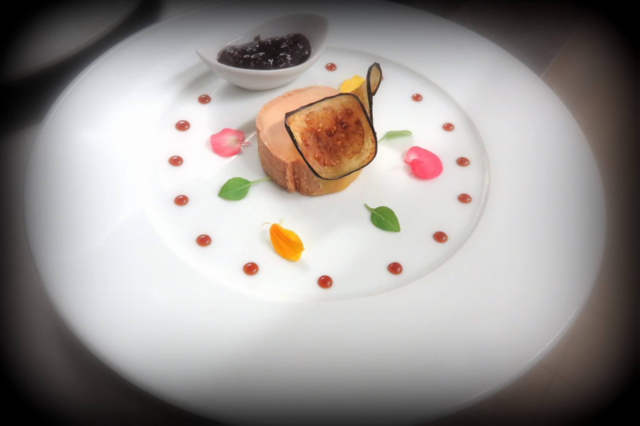 A white plate with a dessert consisting of a slice of cake and a fruit garnish.