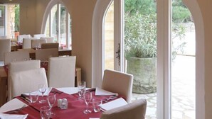 Un comedor con una mesa dispuesta para cuatro, sillas blancas y un camino de mesa rojo. Amplias ventanas arqueadas ofrecen vistas al exterior.
