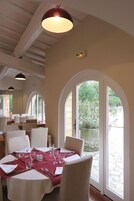 Un comedor con una mesa dispuesta para cuatro, sillas blancas y un camino de mesa rojo. Amplias ventanas arqueadas ofrecen vistas al exterior.