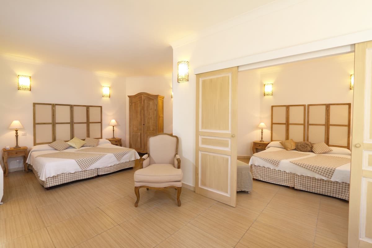 A hotel room with two beds, a wooden wardrobe, a chair, and bedside lamps.