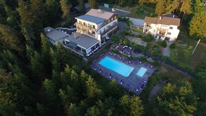 Vue aérienne d’un complexe hôtelier doté d’une grande piscine, de plusieurs bâtiments et entouré d’une forêt dense.