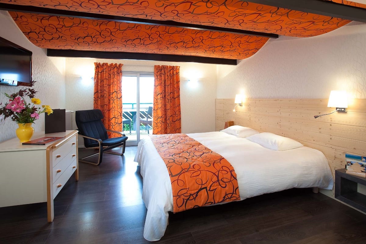 Quarto de hotel com uma cama, uma escrivaninha, uma cadeira e uma mesa pequena com abajur.