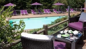 Un espace aménagé au bord de la piscine, avec des chaises longues et des parasols, une terrasse en bois et une table avec un service à thé.