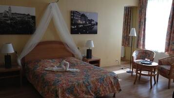 Una habitación de hotel con una cama, dos mesitas de noche, una silla y una pequeña mesa.