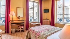 A hotel room with a bed, desk, chair, and a window with a balcony view. - Hôtel du Théâtre (Metz)