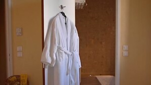 A room with a wooden floor, a white robe hanging on a door, a wooden chair, and a small table with a decorative bowl. - Hôtel du Théâtre (Metz)