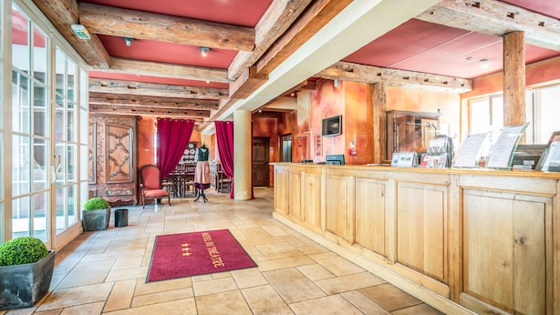 A hotel lobby with wooden beams, a reception desk, a red carpet, and a large window. - Hôtel du Théâtre (Metz)