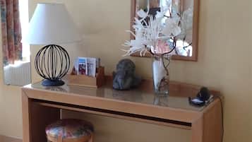 Un escritorio de madera con una lámpara, un florero con flores, un espejo y una silla.