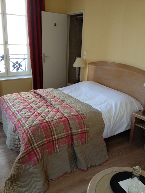 A hotel room with a bed, a wooden headboard, a bedside table, a lamp, and a window with curtains.