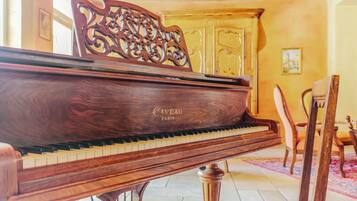 Um piano de cauda com acabamento em madeira e o nome da marca 'Caveau Paris' visível em sua lateral, colocado em um quarto com piso ladrilhado e uma cadeira de madeira ao fundo.