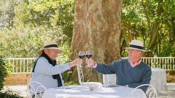 Un área de comedor al aire libre con sillas metálicas blancas y una mesa cubierta con mantel floreado.