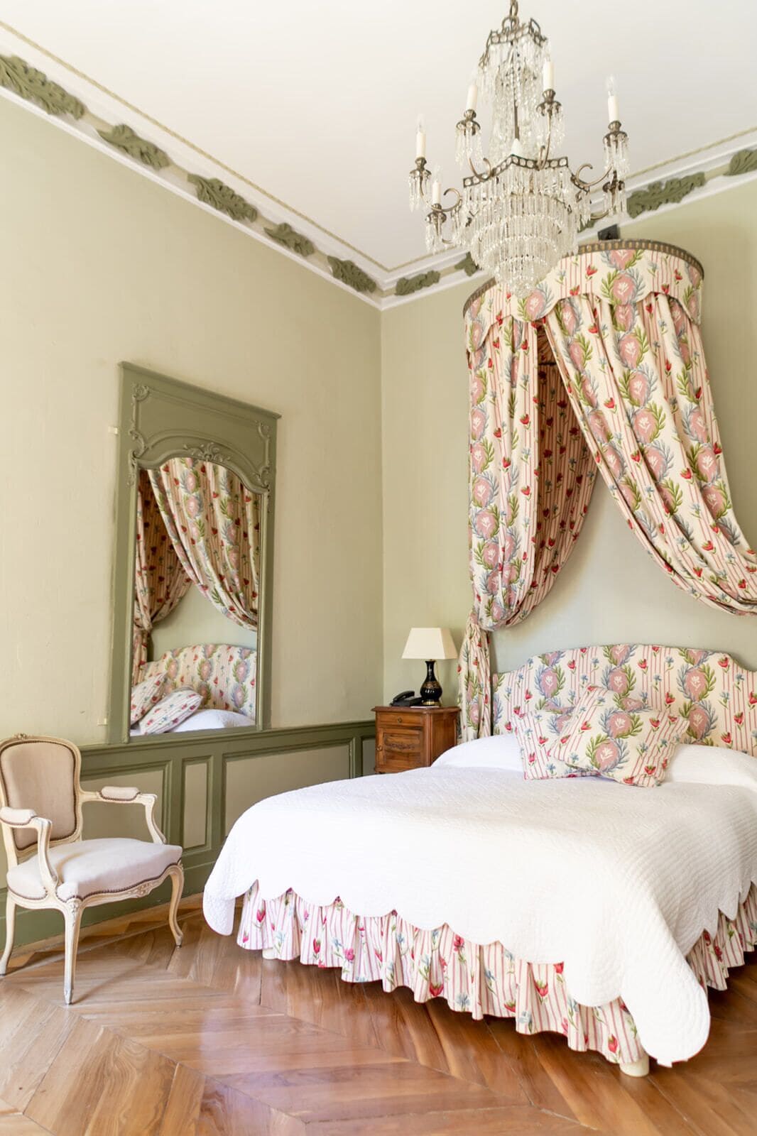 Ein Schlafzimmer mit einem großen Bett, einem Spiegel, einer Chandelieber und blumigen Vorhängen.