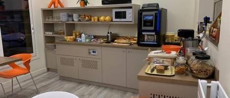 A compact kitchen with modern appliances, a dining area with orange chairs, and a view of the street outside.