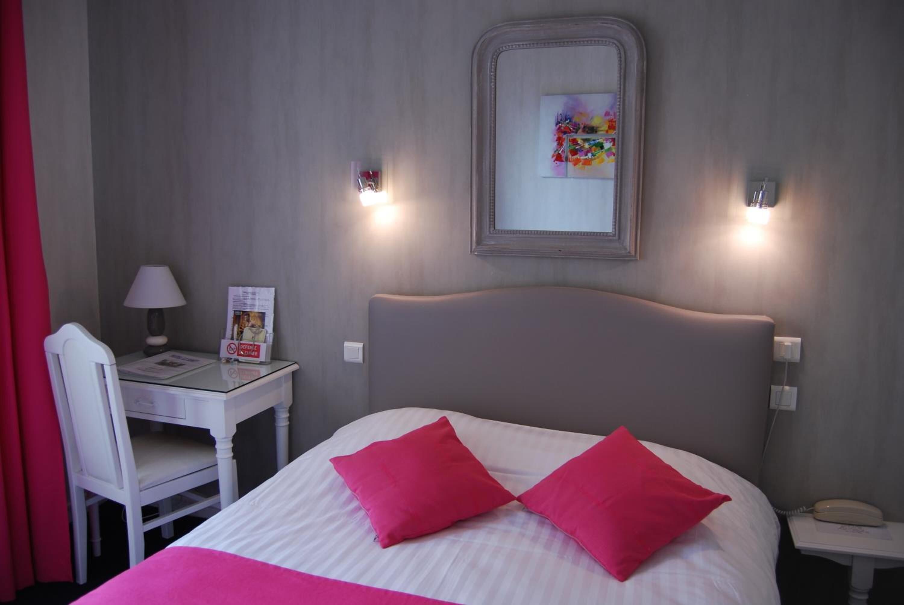 Habitación de hotel con cama, escritorio, silla, teléfono y espejo adosado a la pared.