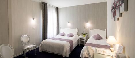 A hotel room with two beds, a chair, a desk with a lamp, and a small table with a plant.