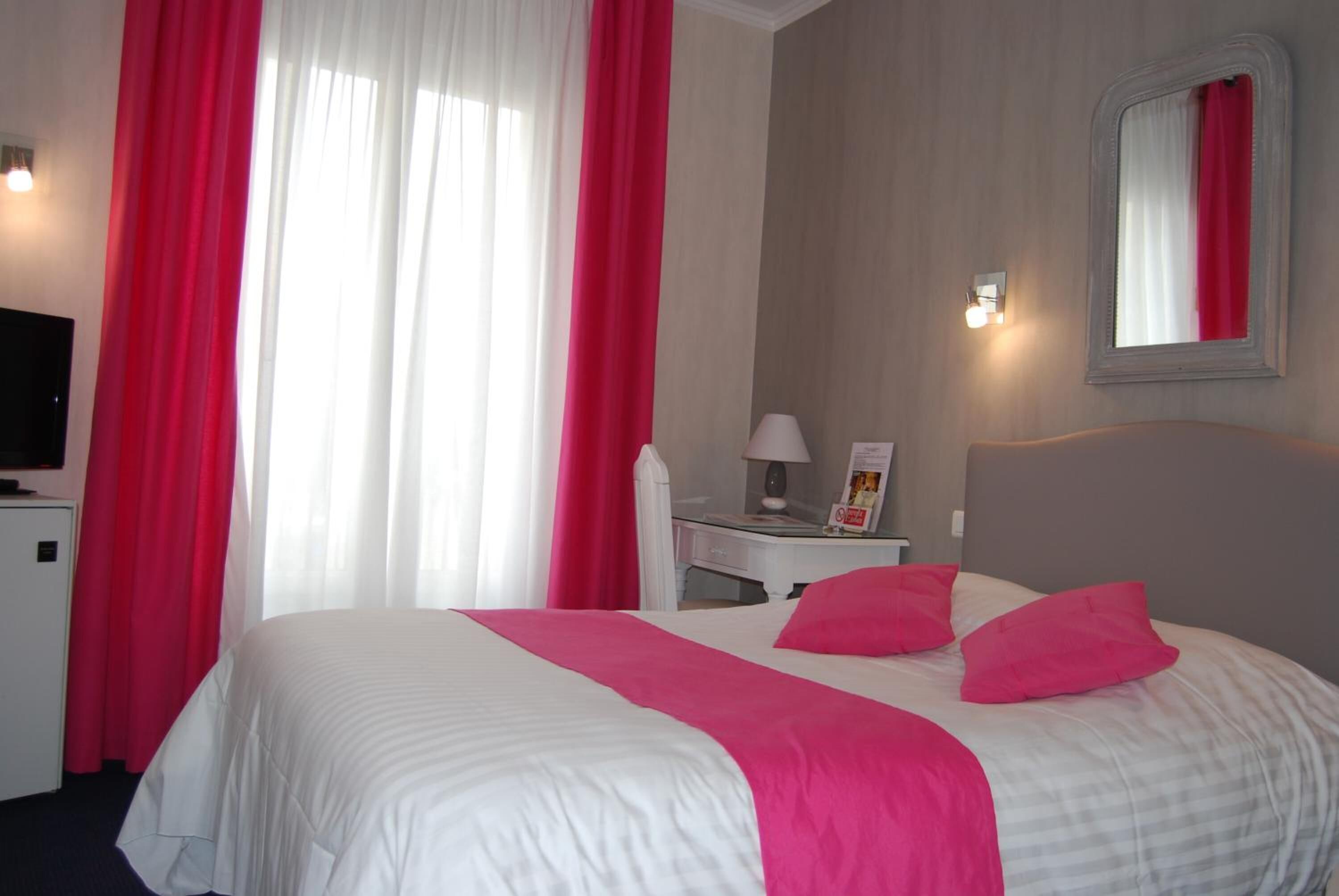 A hotel room with a bed, a desk, a chair, a TV, and a window with curtains.