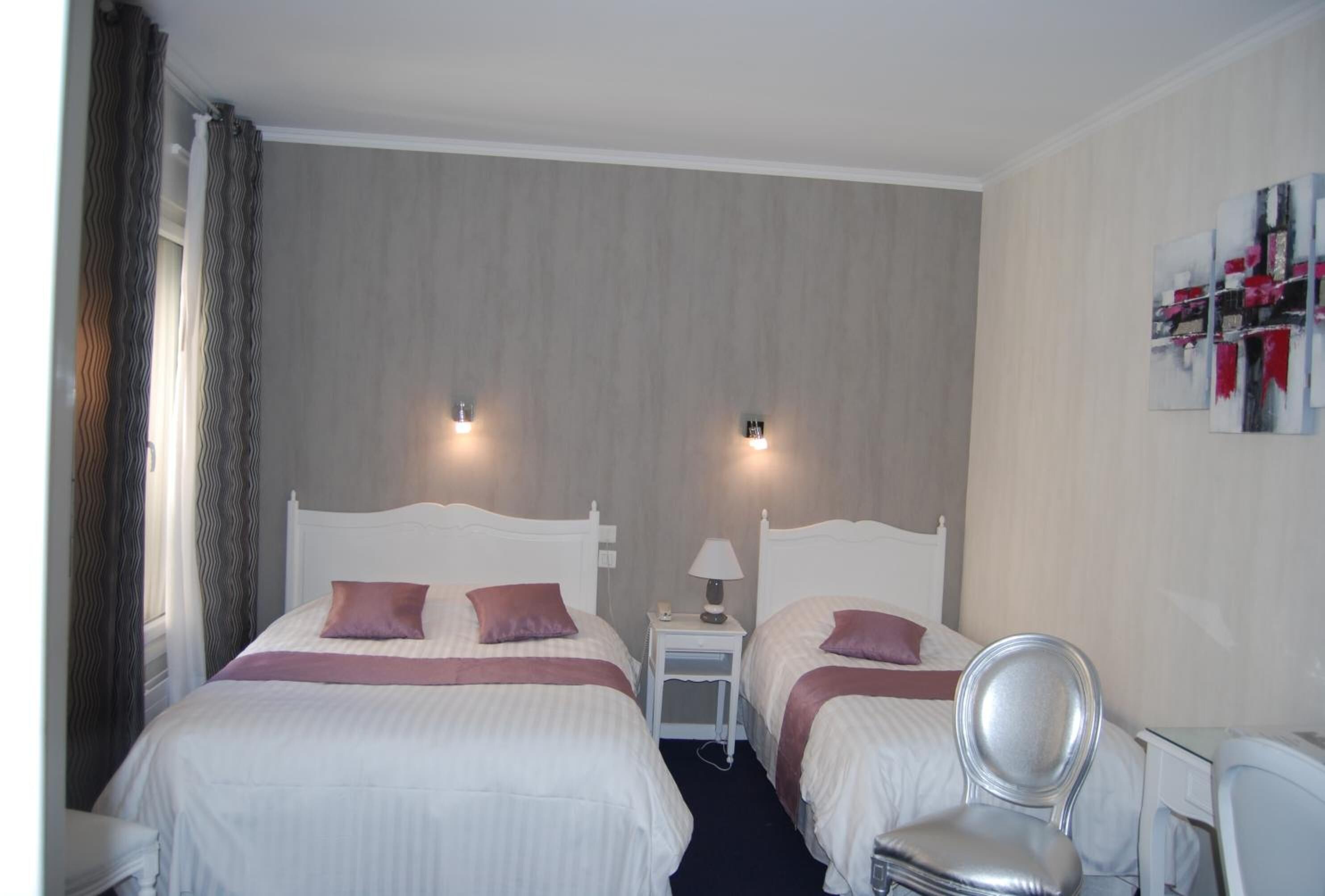 Une chambre d’hôtel avec deux lits, une chaise, une petite table avec une lampe et des œuvres d’art accrochées au mur.