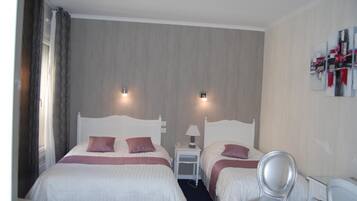 Une chambre d’hôtel avec deux lits, une chaise, une petite table avec une lampe et des œuvres d’art accrochées au mur.