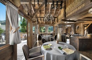 A restaurant with wooden beams, large windows, and a chandelier. Tables are set with plates, glasses, and cutlery. - Hotel Restaurant La Bouitte - Relais & Châteaux - 2 étoiles Michelin (Les Belleville)