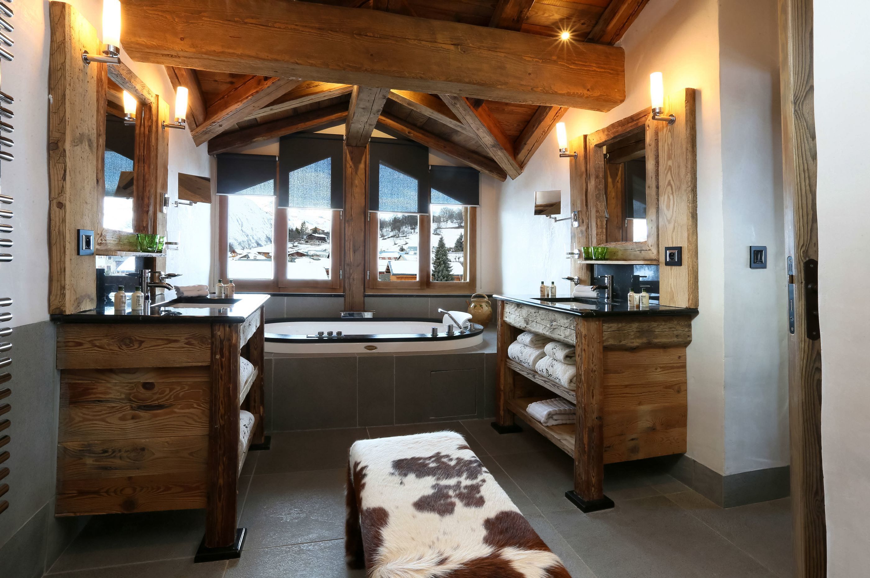 Une salle de bain avec des poutres en bois, une grande baignoire et une fenêtre donnant sur un paysage enneigé.