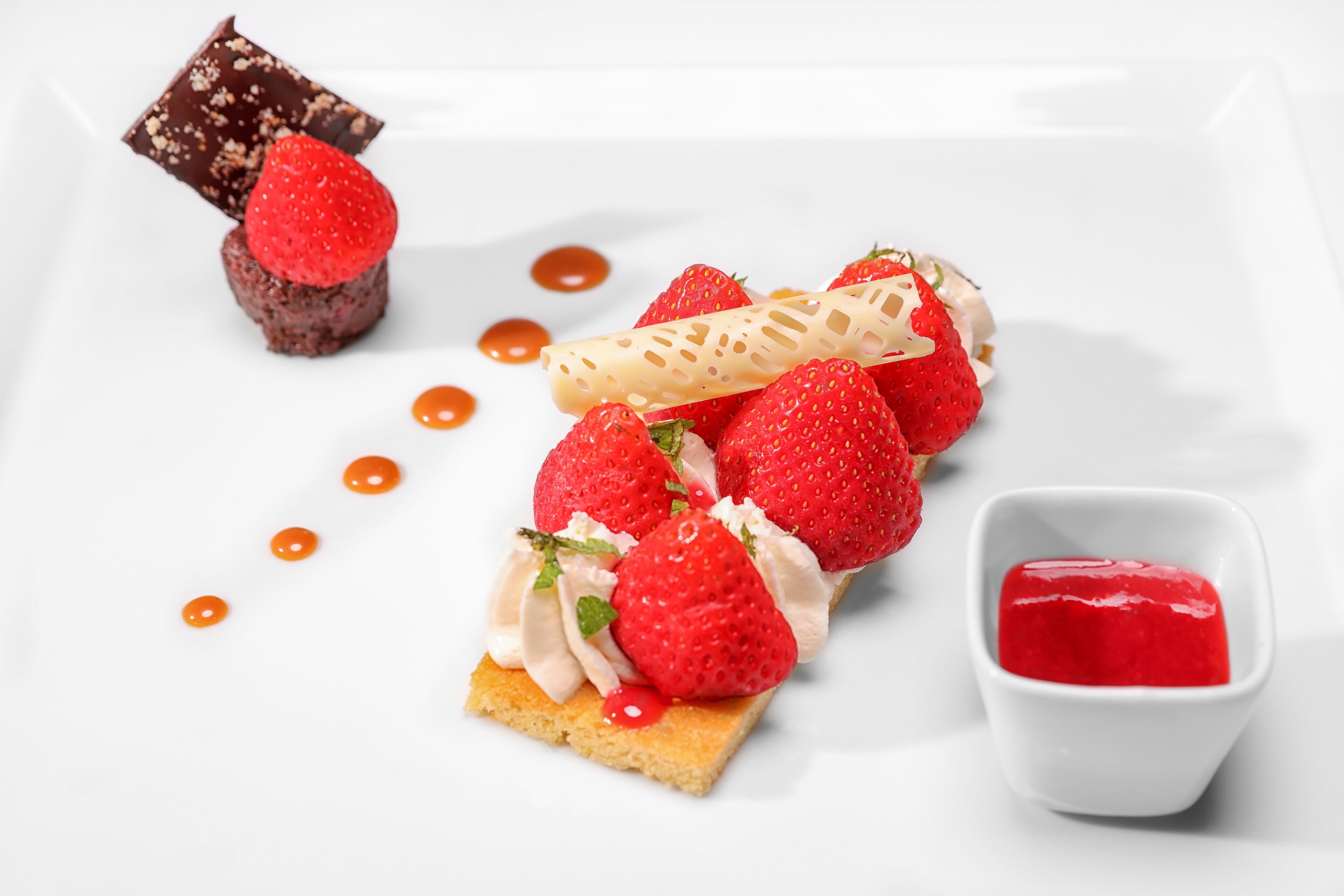 Un plato de postre con fresas, crema batida y chocolate.