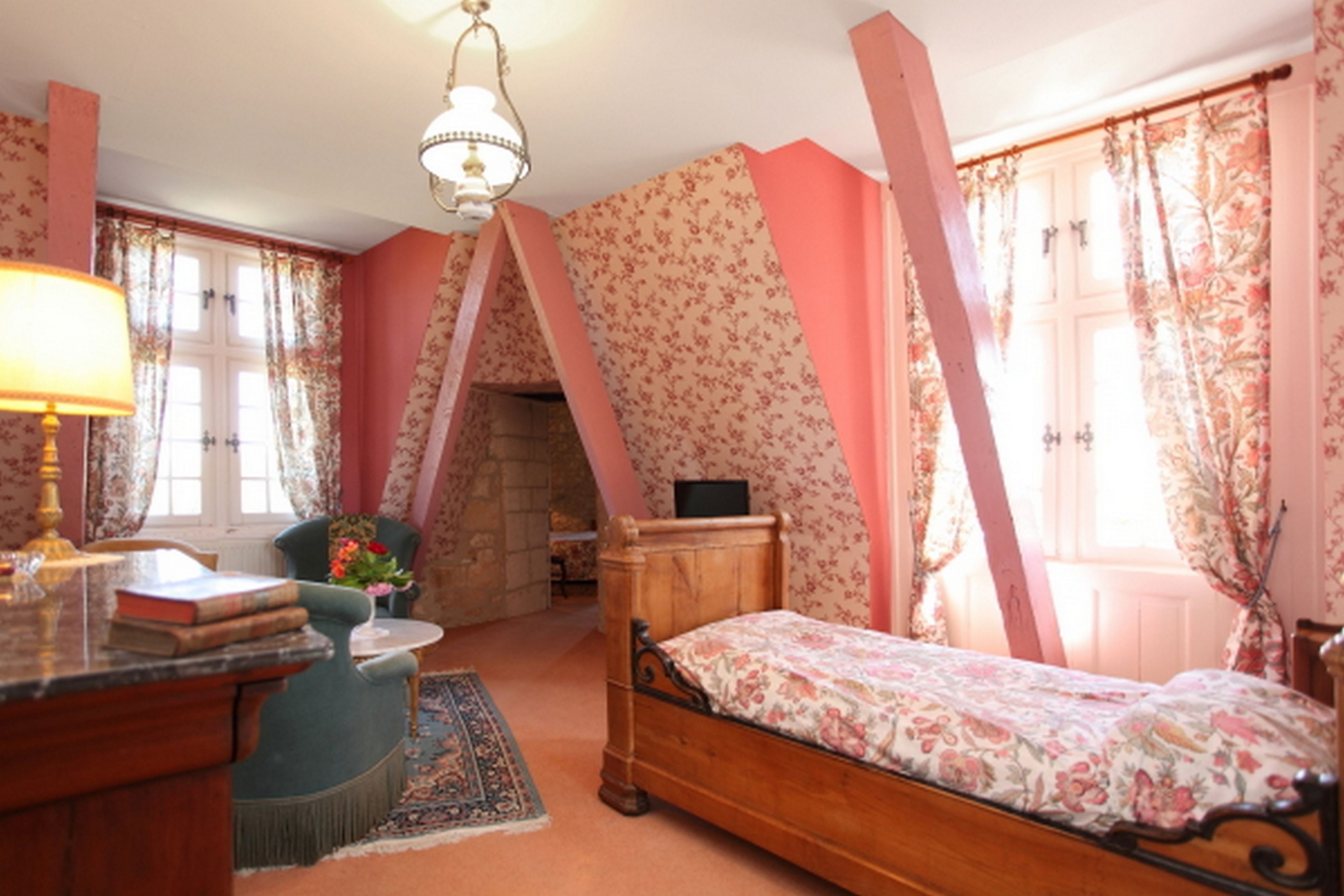 A bedroom with a bed, a desk, a chair, a lamp, and a fireplace.