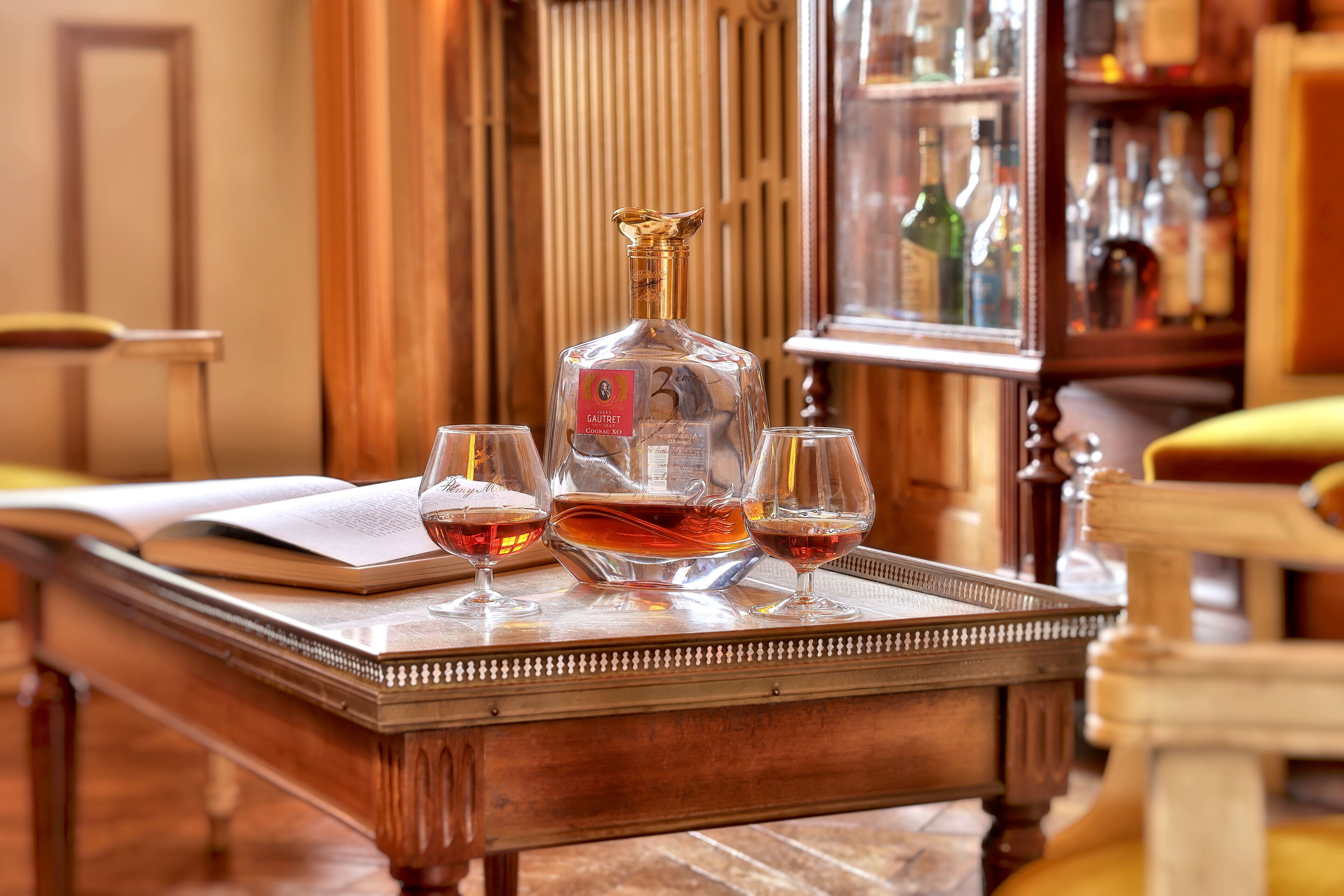 A wooden table with a bottle and three glasses of whiskey, a book, and a tray.