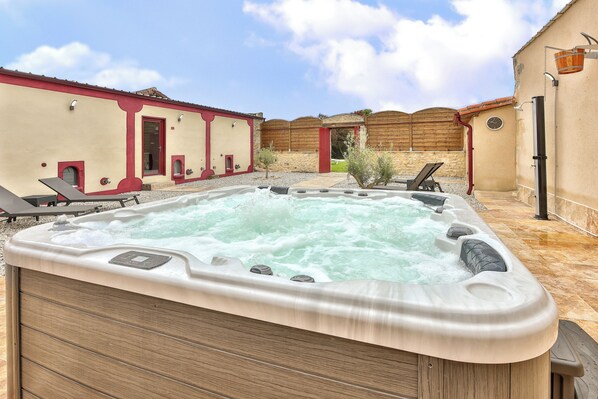 A hot tub in a courtyard with a beige building, a wooden fence, and a clock on the wall.