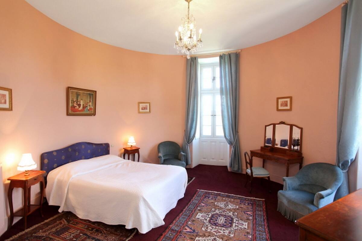 Une chambre à coucher avec un lit, un bureau, une chaise, un lustre et une fenêtre avec des rideaux.