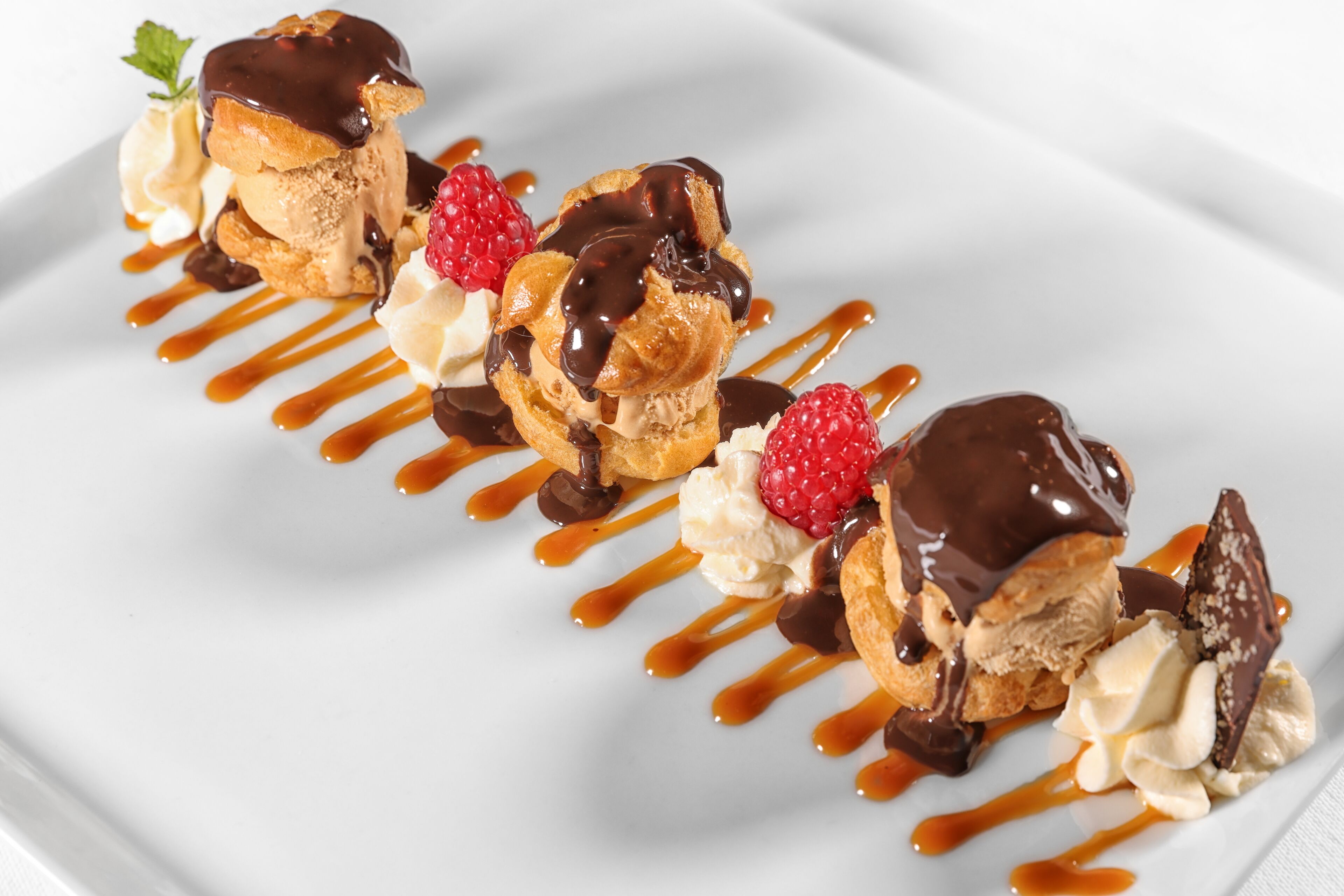 A dessert plate with éclairs, whipped cream, raspberries, and chocolate sauce.