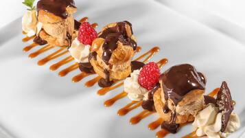 A dessert plate with éclairs, whipped cream, raspberries, and chocolate sauce.