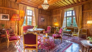 A traditional room with wooden paneling, a chandelier, red upholstered chairs, a patterned rug, and framed pictures on the walls. - Hôtel & Spa Château de La Côte - Brantôme (Biras)