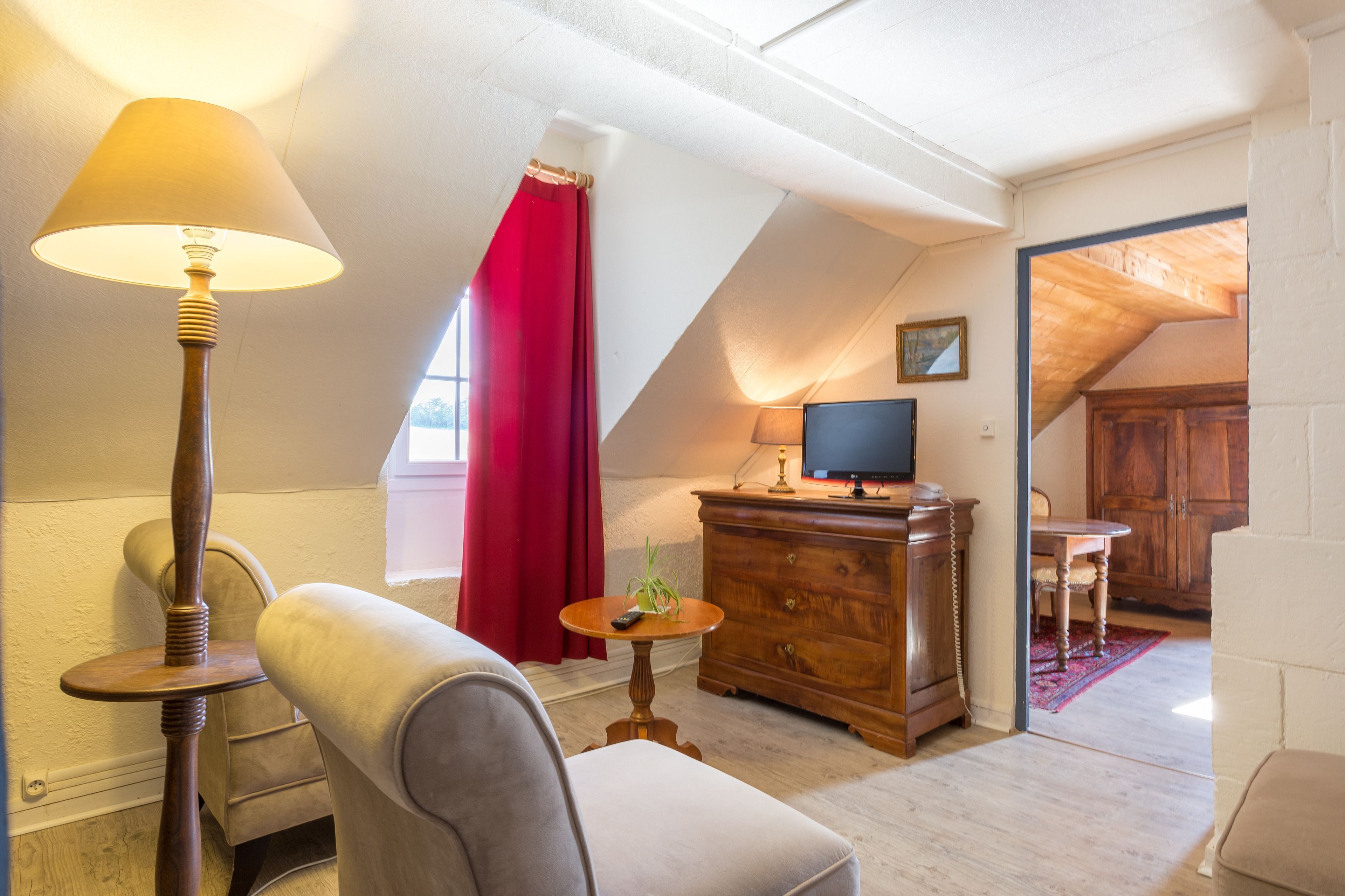 A cozy room with a sloped ceiling, a wooden cabinet, a television, a red curtain, and a lamp.