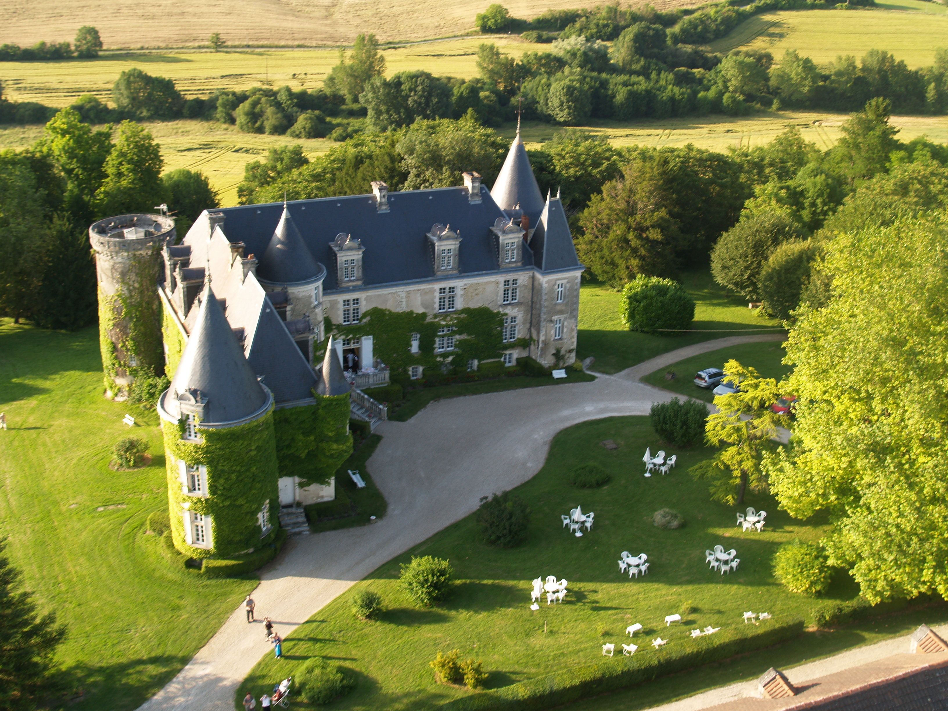 Une vue aérienne d’un vaste domaine comprenant un imposant bâtiment qui ressemble à un château, une pelouse bien entretenue et plusieurs espaces aménagés pour se détendre en plein air.