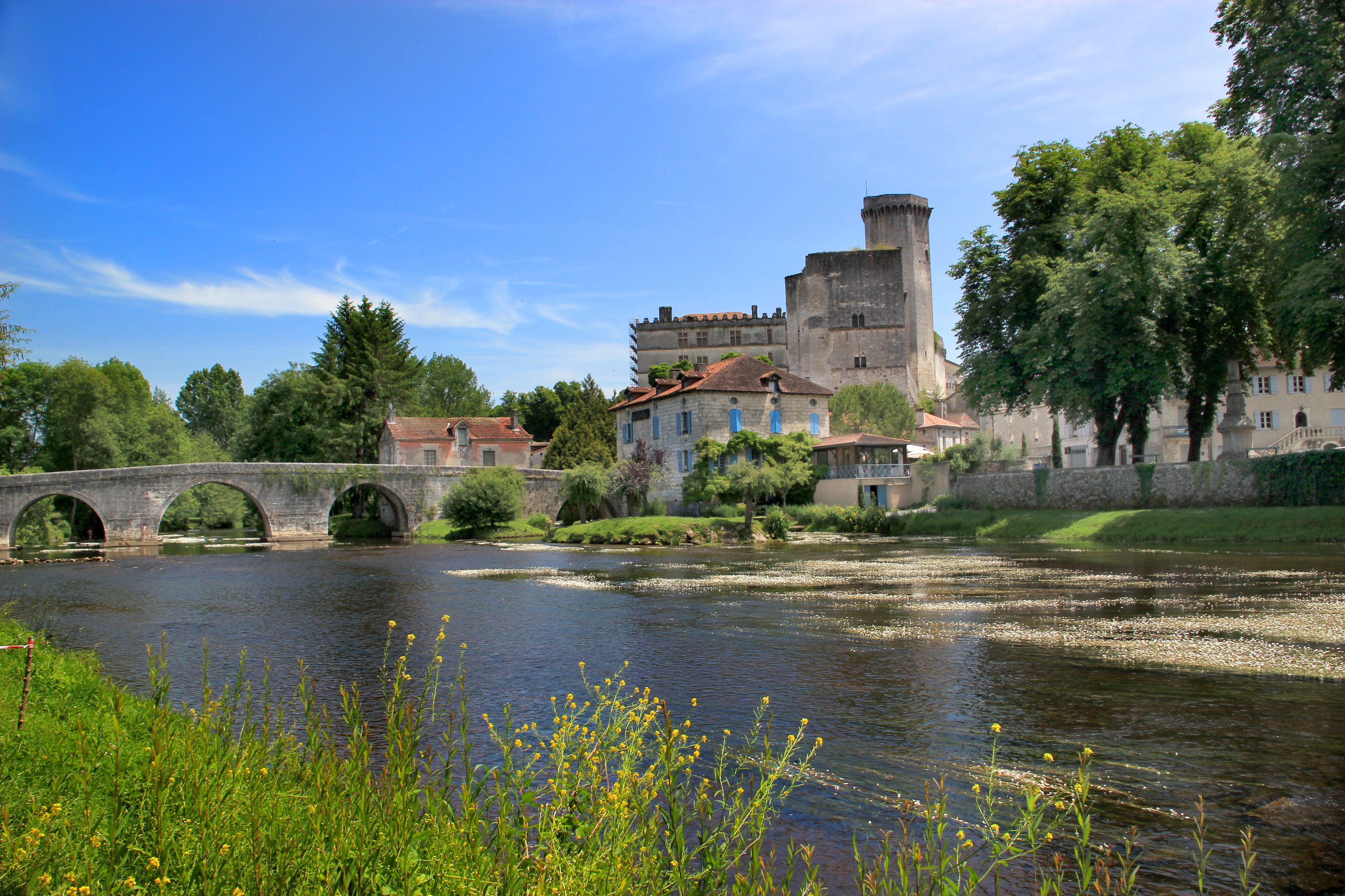 A historic stone bridge over a river, a castle-like building, and lush greenery.