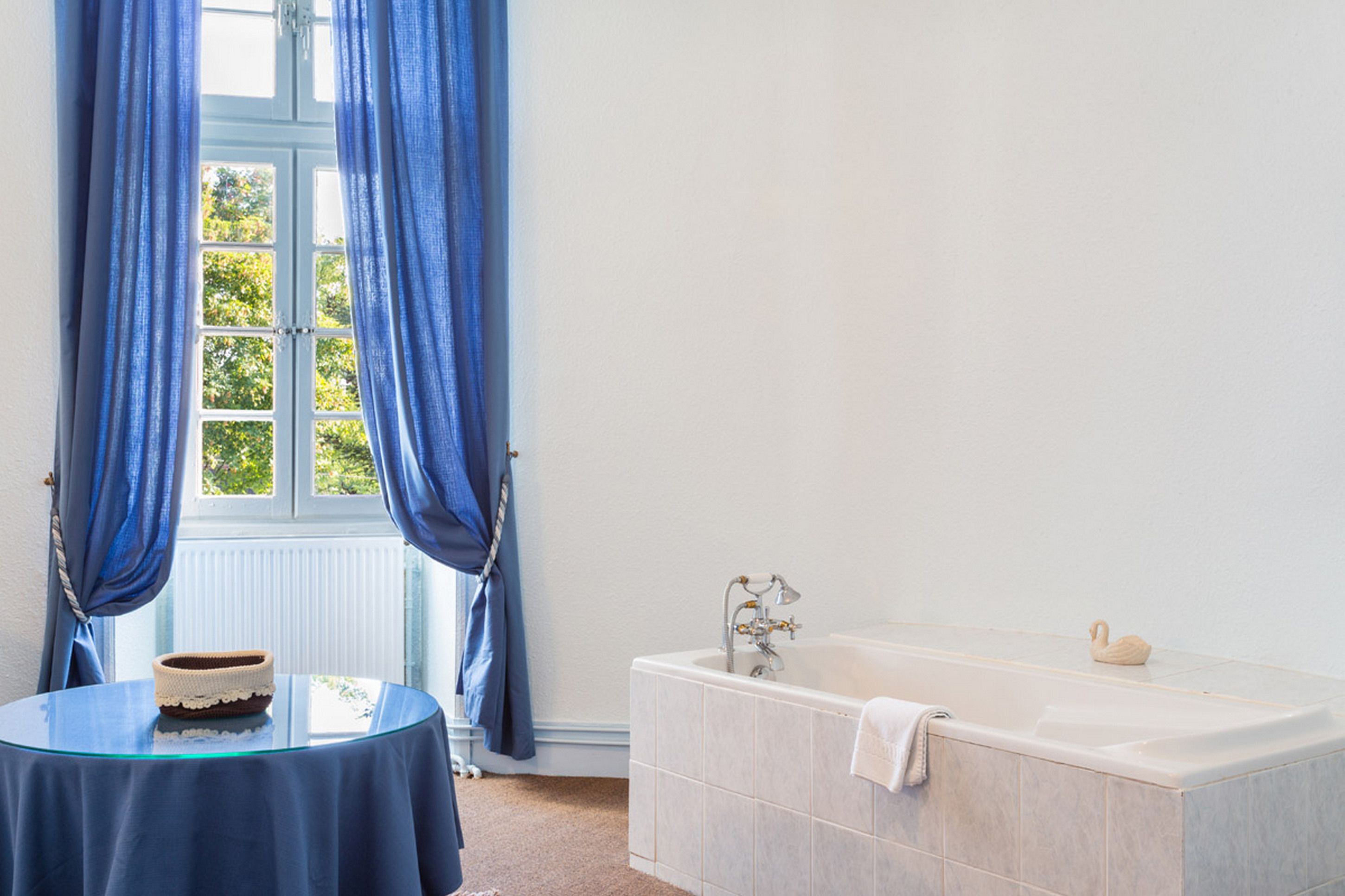 Une salle de bain avec une baignoire, une table avec un panier, et des rideaux bleus.