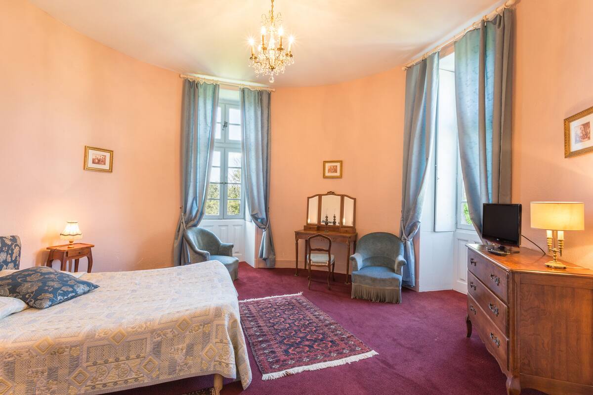 Une chambre à coucher comprenant un lit, deux chaises, une commode, un bureau, un téléviseur et un lustre.