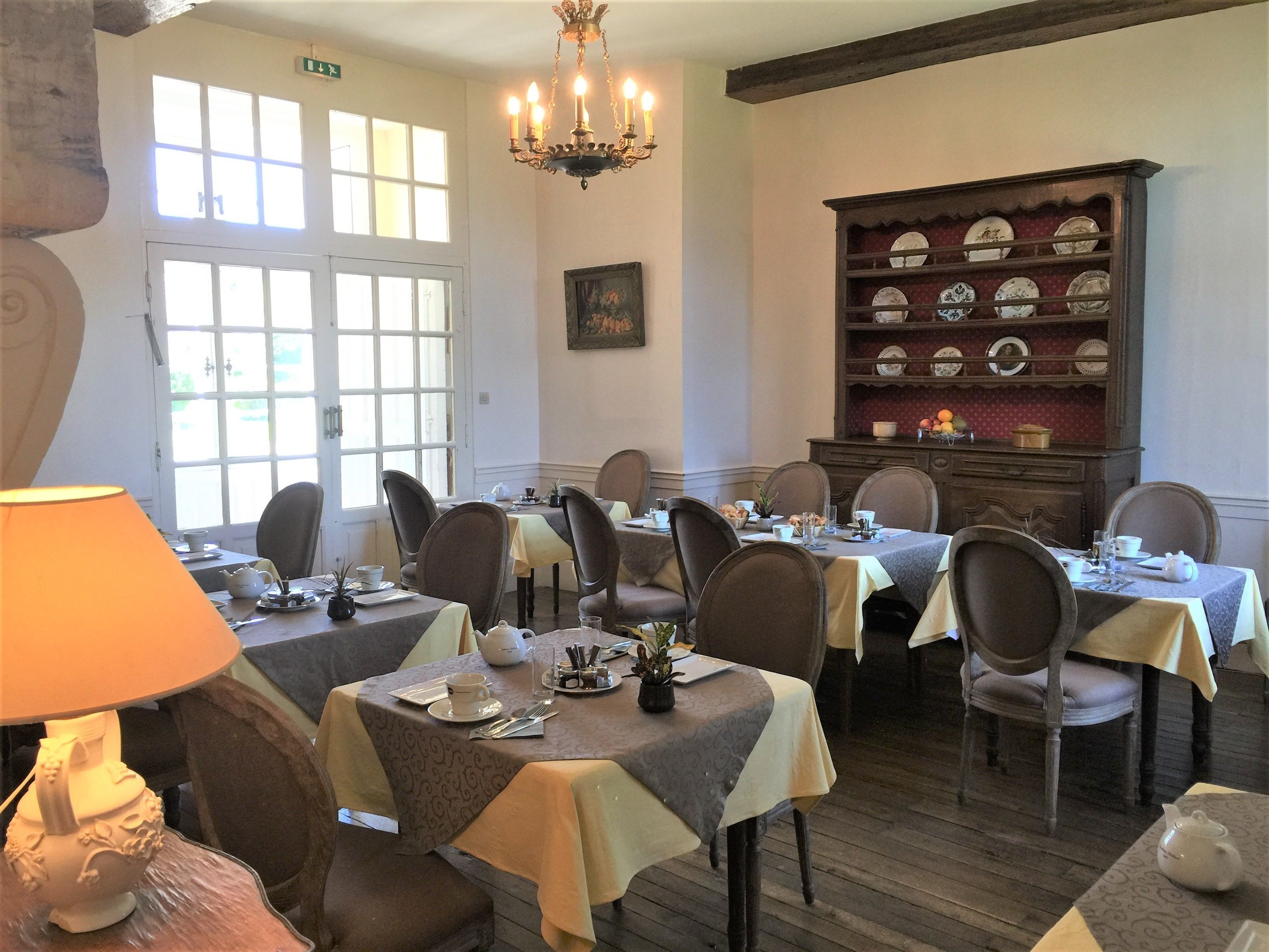 Een eetkamer met gedekte tafels, stoelen, een kroonluchter en een vitrinekast.