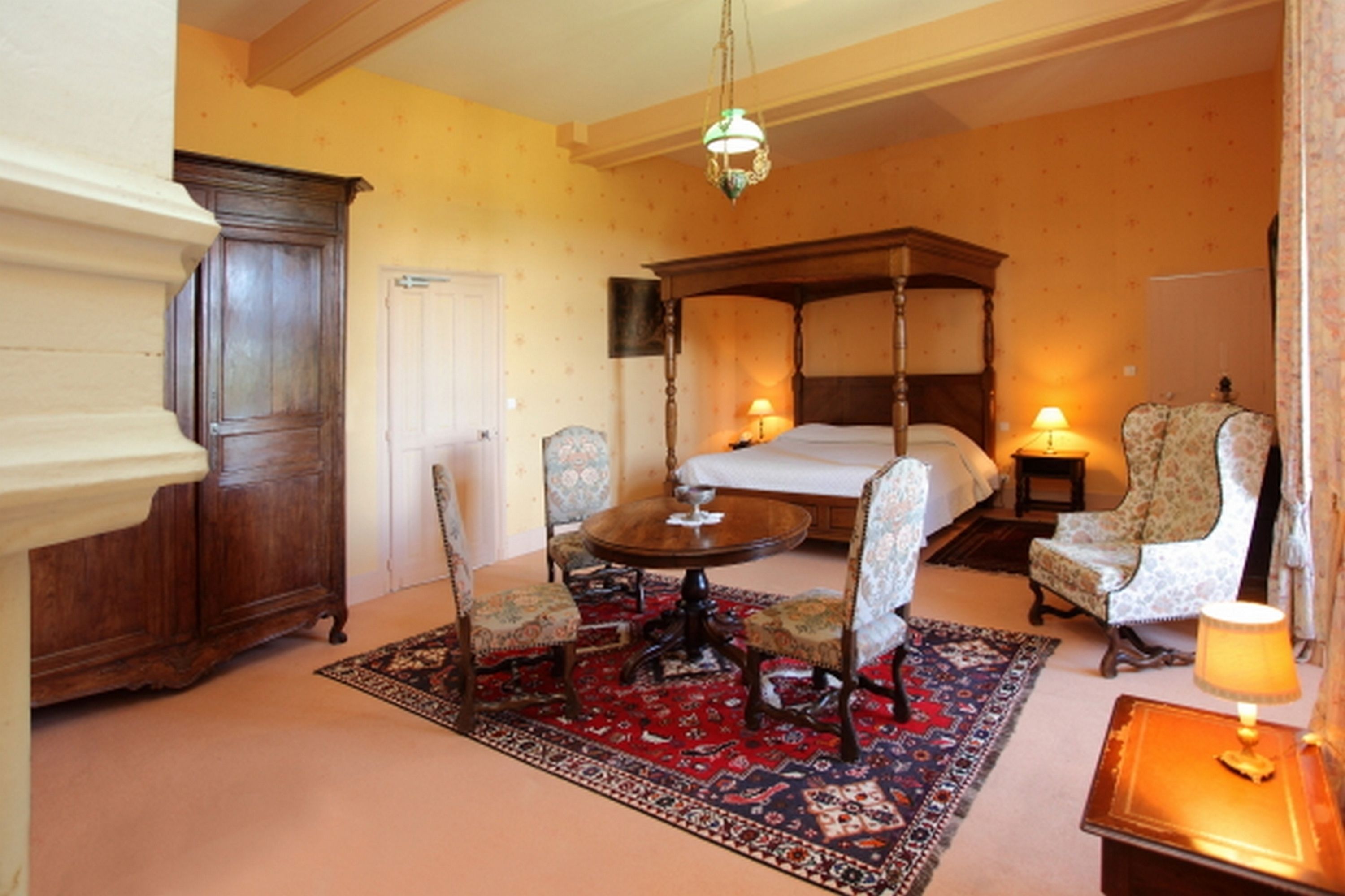 A traditional room with a four-poster bed, a wooden cabinet, a round table with chairs, and a patterned rug.