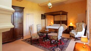 A traditional room with a four-poster bed, a wooden cabinet, a round table with chairs, and a patterned rug.